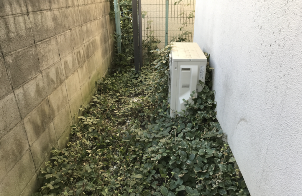 周りが雑草で覆われているエアコン室外機の画像